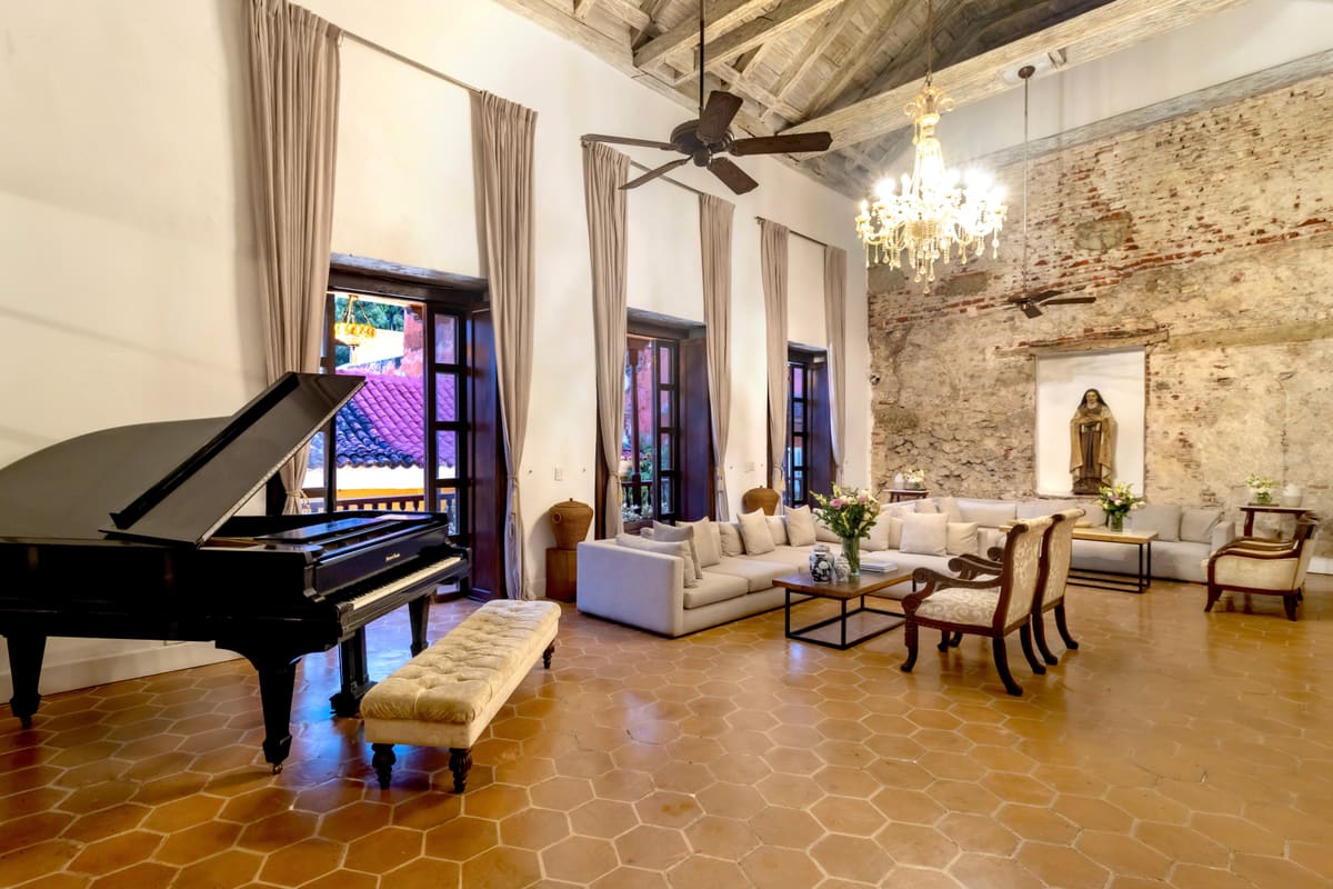 Sala con piano de cola, candelabro y muros coloniales